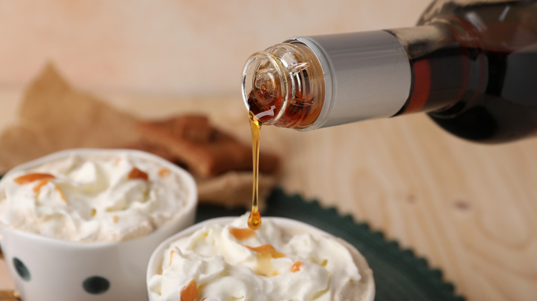 Caramel syrup is being poured onto coffee topped with whipped cream