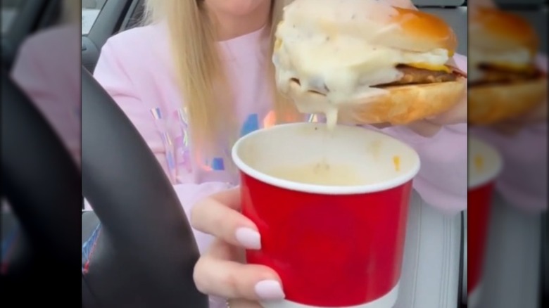 A person in a car dipping a sandwich into a cup of gravy