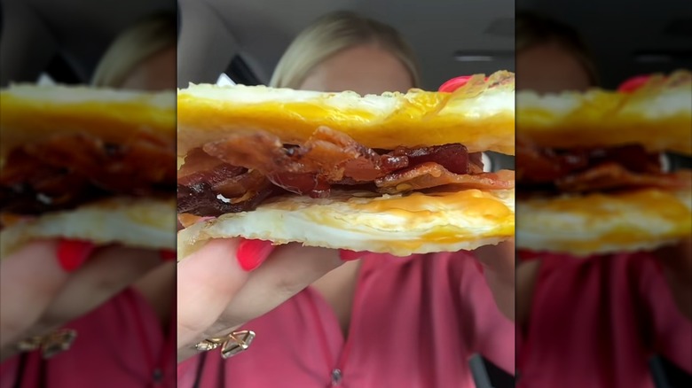 A person holding bacon sandwiched between two egg patties