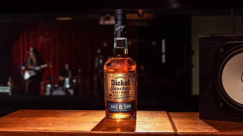 A bottle of George Dickel 8-year on a table with a band playing in a blurred background