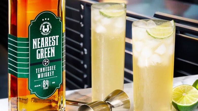 A bottle of Uncle Nearest Tennessee Whiskey shown next to two cocktails and some cut lime