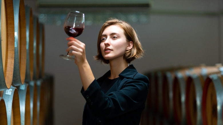 a woman inspecting a glass of red wine in a cellar