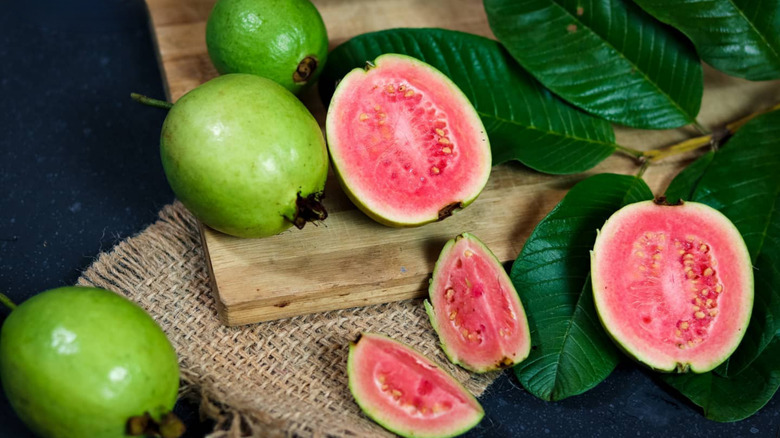 halved and whole guavas on leaves, wood, and woven towel