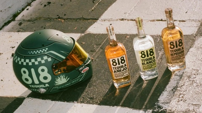 All three 818 tequila expressions shown on the floor beside a branded racing helmet