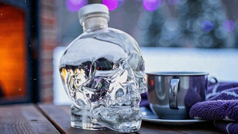 A bottle of Crystal Head Vodka on a table placed beside a metal cup