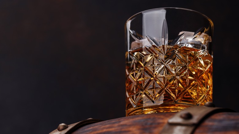 A close up of a full glass of whiskey perched on top of a barrel