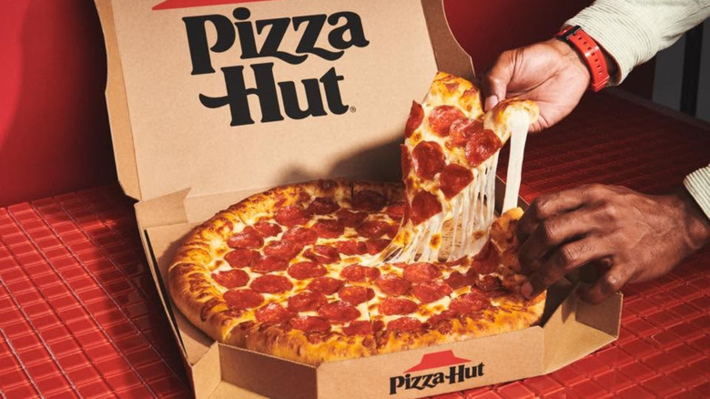 Hands pulling slice of Pizza Hut stuffed-crust pizza out of cardboard box.