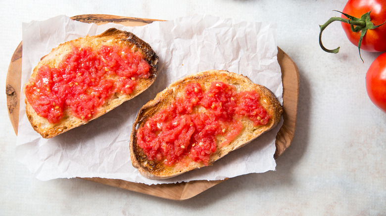 Two pan con tomate on lined wooden board with tomatoes on the side
