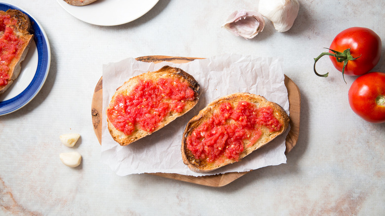 pan con tomate on board surrounded by tomatoes and garlic
