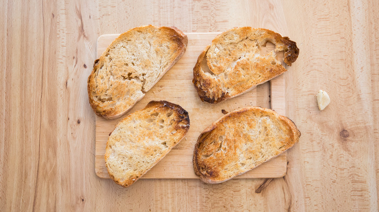 four slices of toasted bread on wooden table next to garlic clove