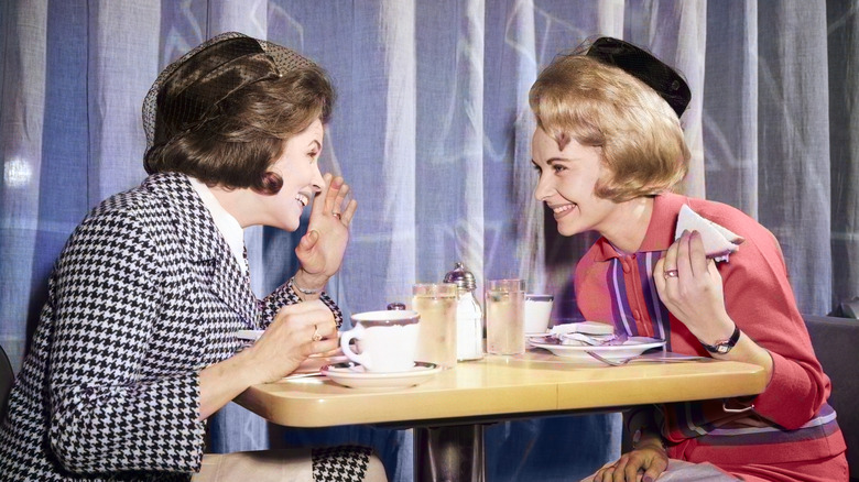 Two women dressed in 1960s fashion talking in a restaurant