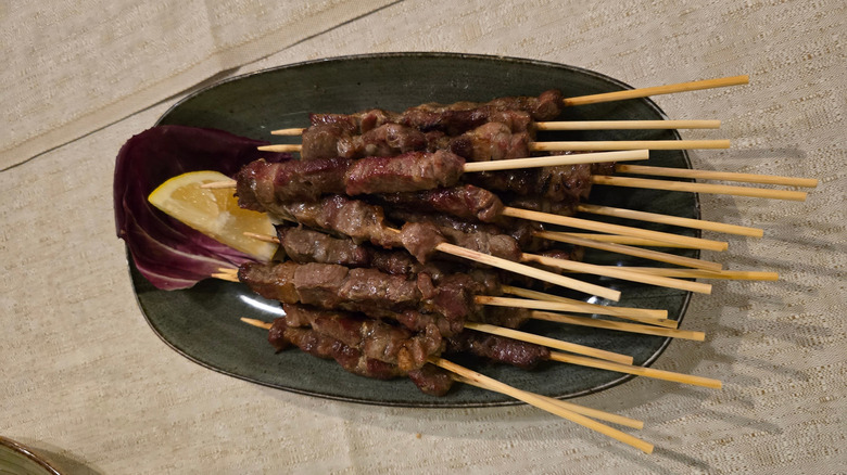 plate of Arrosticini on wooden skewers on dark plate