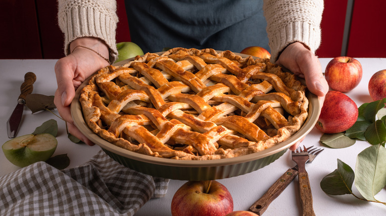 Hands holding freshly baked apple pie over decorated table.