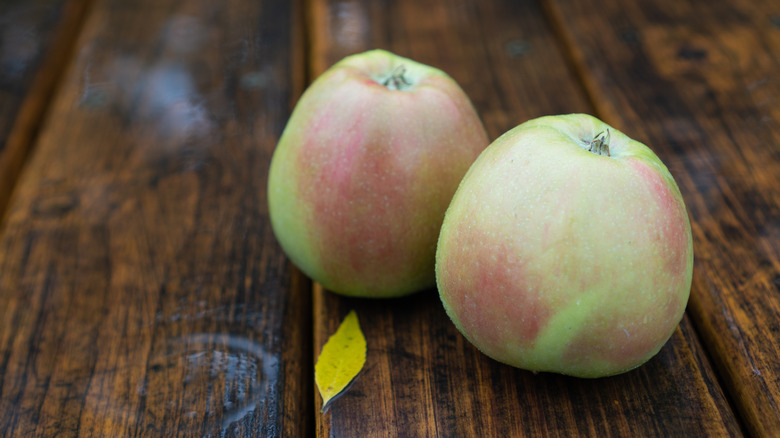 Two Northern Spy apples on a wooden table.