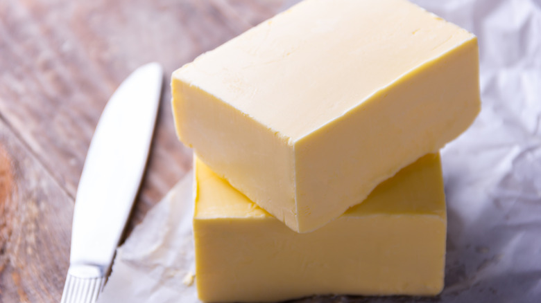 Two cubes of butter alongside a knife on a wooden table