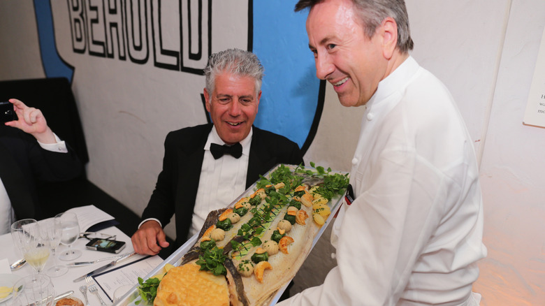 Anthony Bourdain looking at a seafood dish garnished with fresh herbs