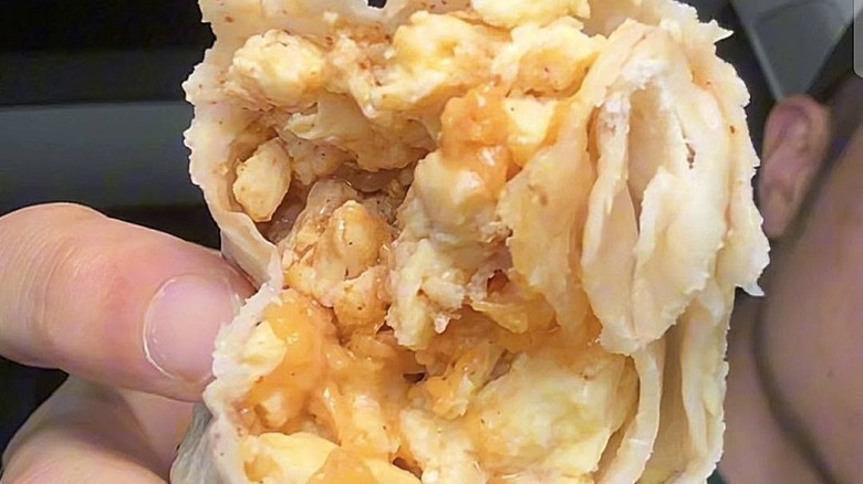 Someone holding a bitten egg and cheese burrito from Del Taco