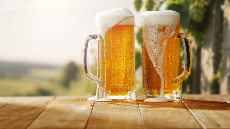 Two foaming beer mugs on wooden table with blurred background