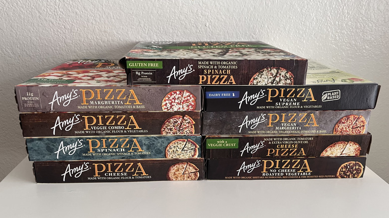 Different flavors of Amy's pizzas stacked on table against a white wall