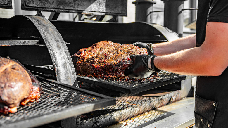 Hands placing meat in a BBQ smoker
