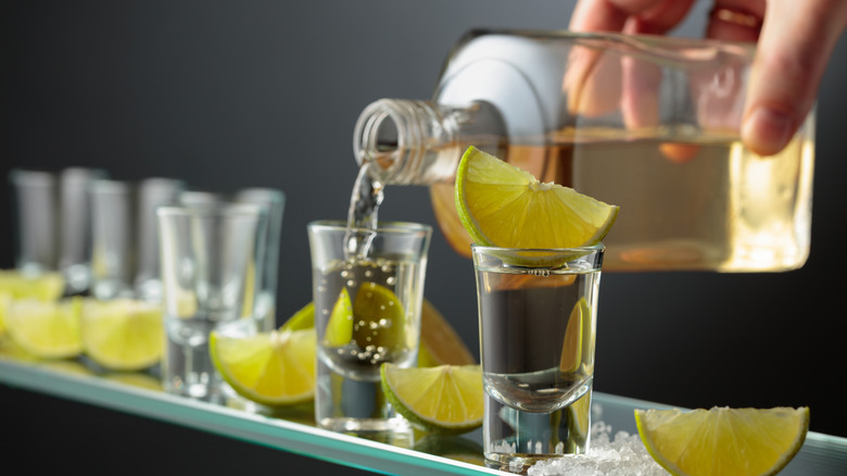 Hand pouring tequila shots with lime