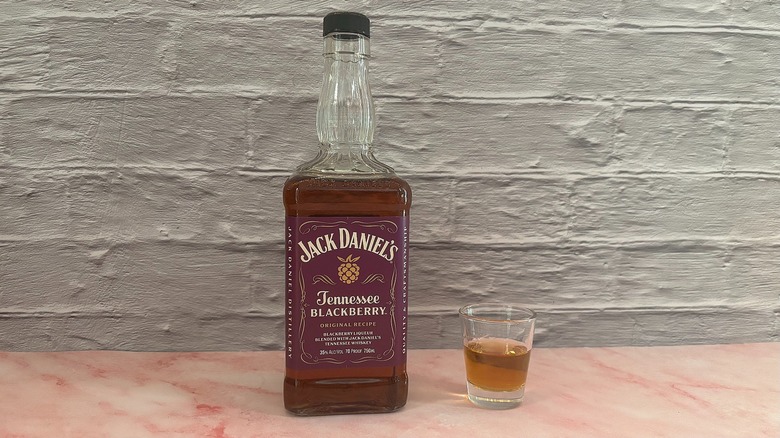 Bottle of Jack Daniel's Tennessee Blackberry  next to shot glass of whisky on grey brick background