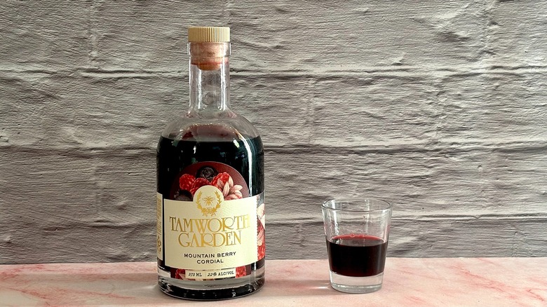 Bottle of Tamworth Garden Mountain Berry Cordial next to shot glass of liqueur on grey brick background