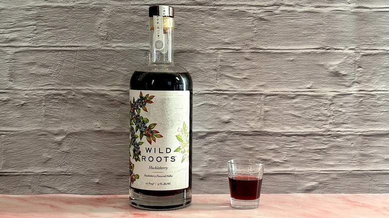 Bottle of Wild Roots Huckleberry Vodka next to shot glass of vodka on grey brick background