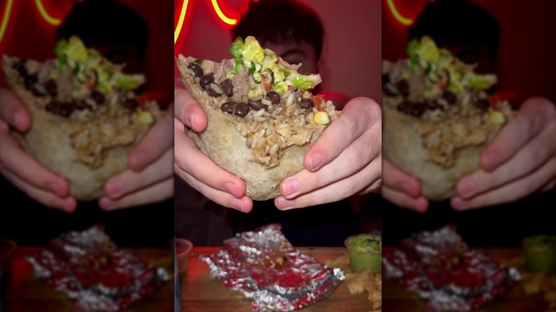 Person holding half-eaten Chipotle barbacoa and brown rice burrito