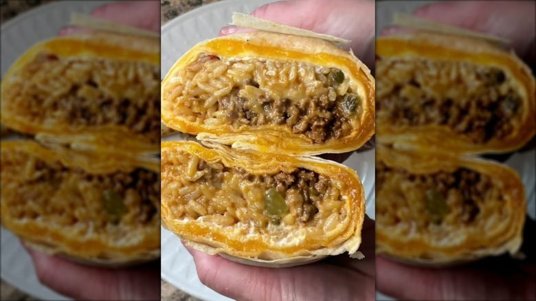 Hands holding halved cheesy burrito, showing meat and rice fillings inside