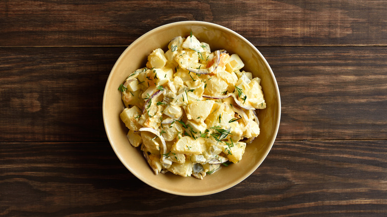 Potato salad in yellow bowl on wooden table