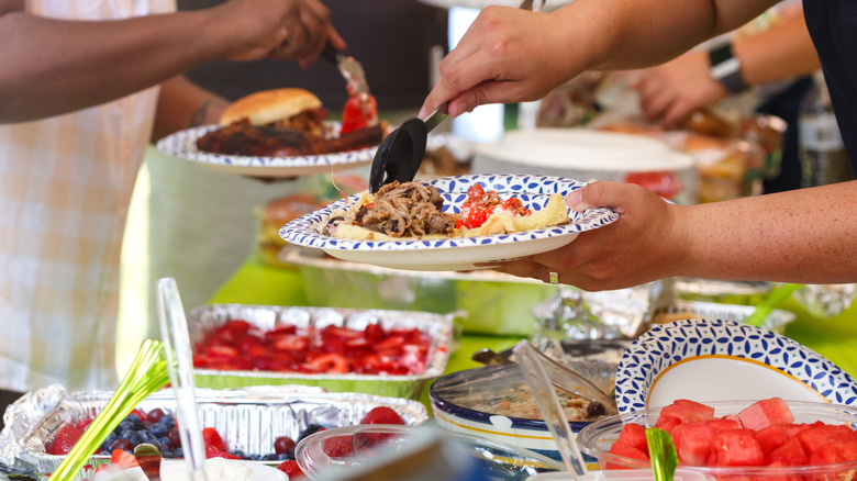 People serving themselves potluck food on paper plates