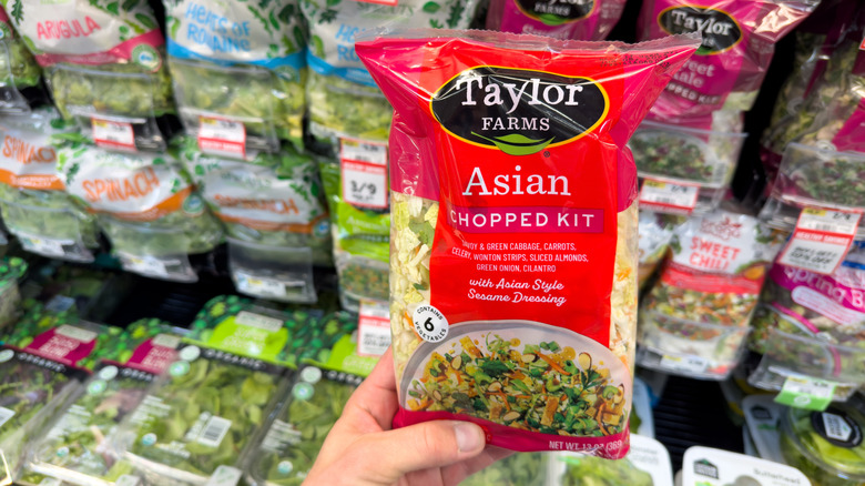 Hand holding bagged salad kit in grocery store