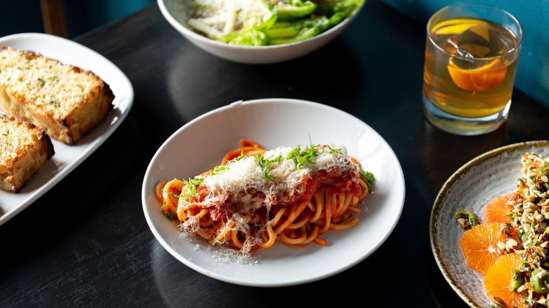 Spaghetti noodles and red sauce topped with finely grated cheese on a white plate, surrounded by toasted bread and salad