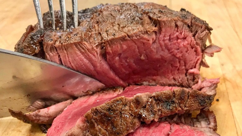 Knife cutting into pink, juicy prime steak on wooden board