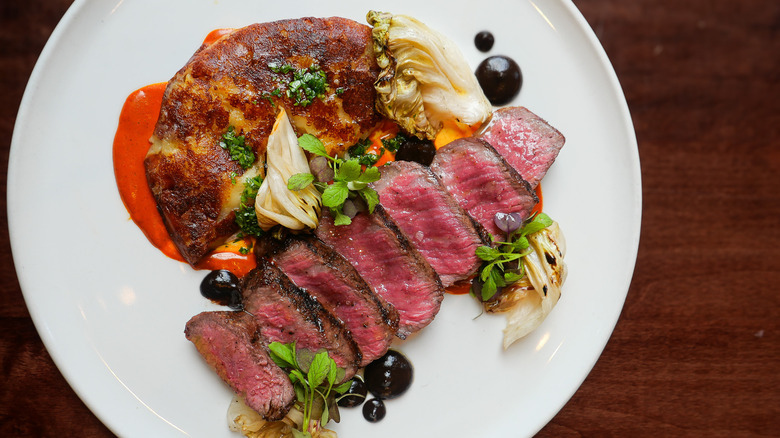 Juicy, pink steak and charred vegetables with dollops of black sauce on white plate