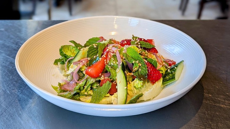 Salad of cucumbers, strawberries, pickled red onions, and fresh herbs in white bowl