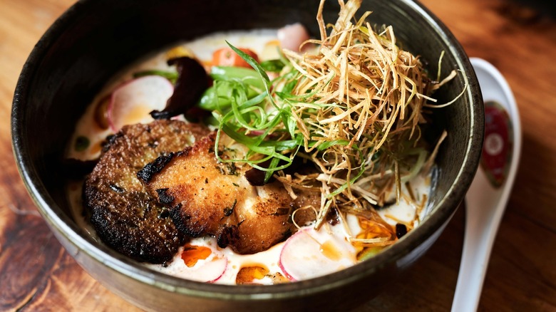 Bowl filled with white meat, creamy broth, sliced radishes, and grass-like topping