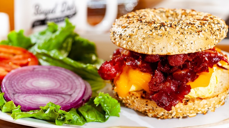 Bagel sandwich with dripping egg, side of sliced red onions, tomato, and lettuce