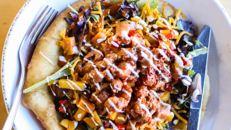 Fry bread topped with shredded meat, cheese, veggies, and drizzled with crema