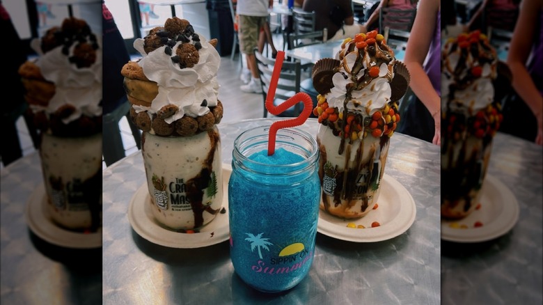 Two towering milkshakes and iced beverage on table