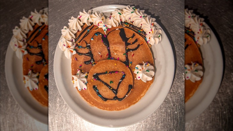 Pancakes decorated with whipped cream, chocolate syrup, and sprinkles to resemble a cartoon bear's face