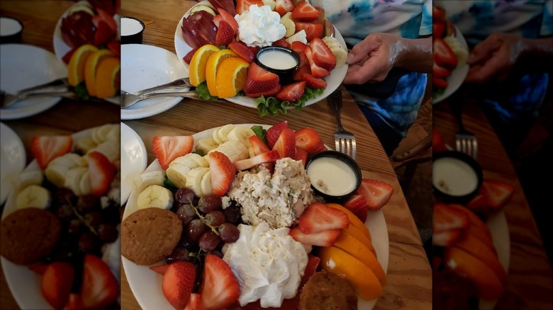 Two plates of food on table with plenty of fruit