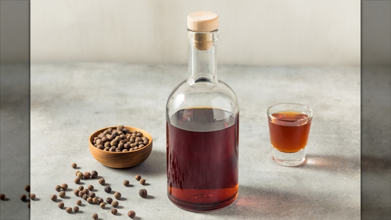 Allspice dram in glass bottle next to allspice berries