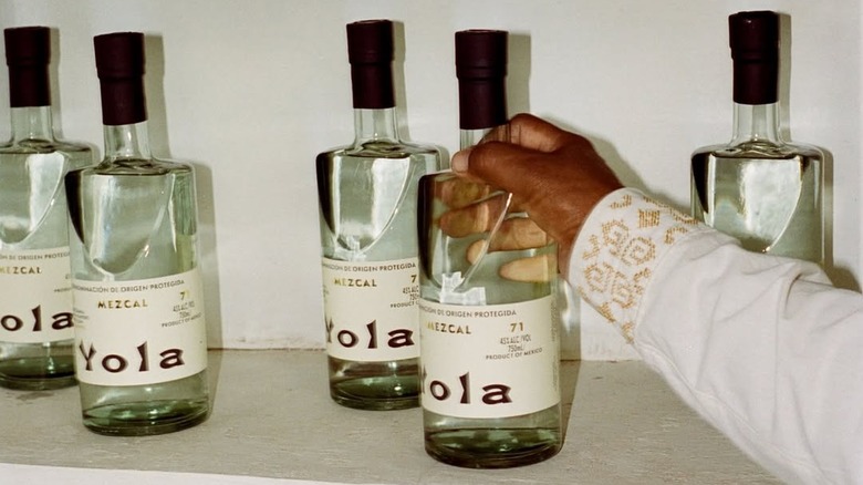 Person grabbing bottles of Yola mezcal from shelf