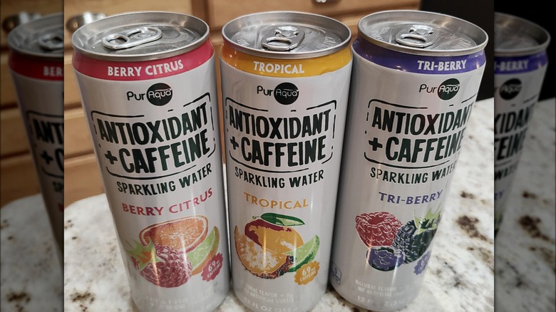 Three cans of Pur Aqua's caffeinated sparkling water in different flavors