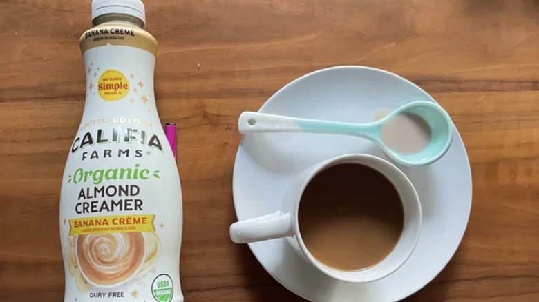 A bottle of Califia Farms creamer sits next to a cup of coffee in a saucer