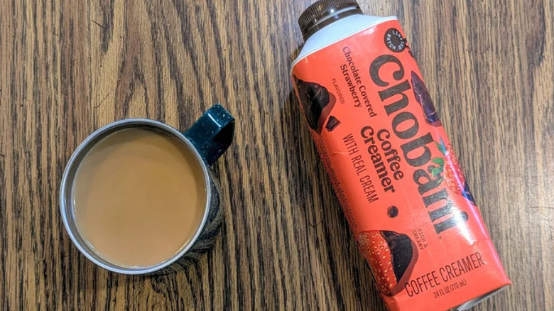 A cup of coffee and a container of Chobani creamer on a woodgrain surface