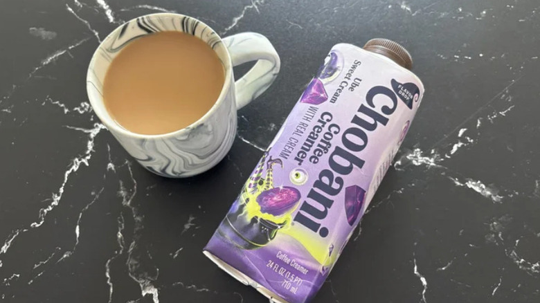 A cup of coffee sits near a container of purple Chobani coffee creamer