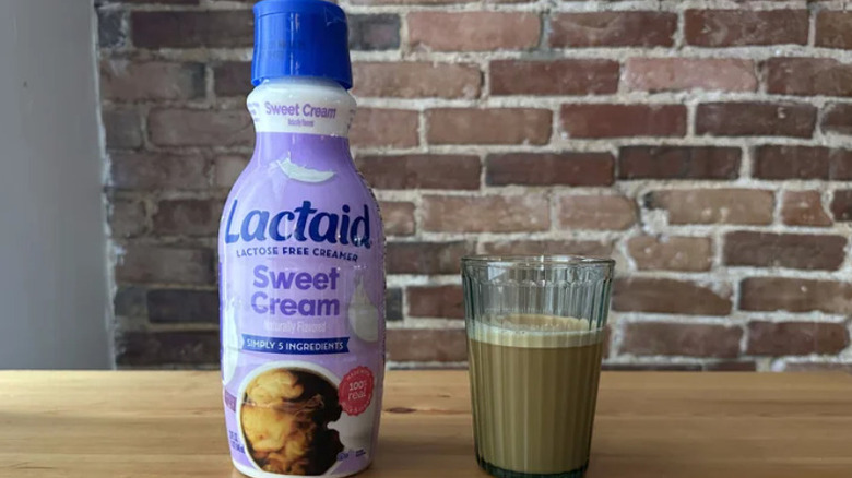 A bottle of Lactaid coffee creamer and a glass of coffee in front of a brick wall
